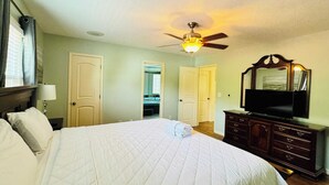 A bedroom with a large bed, a ceiling fan, a dresser, and a television.