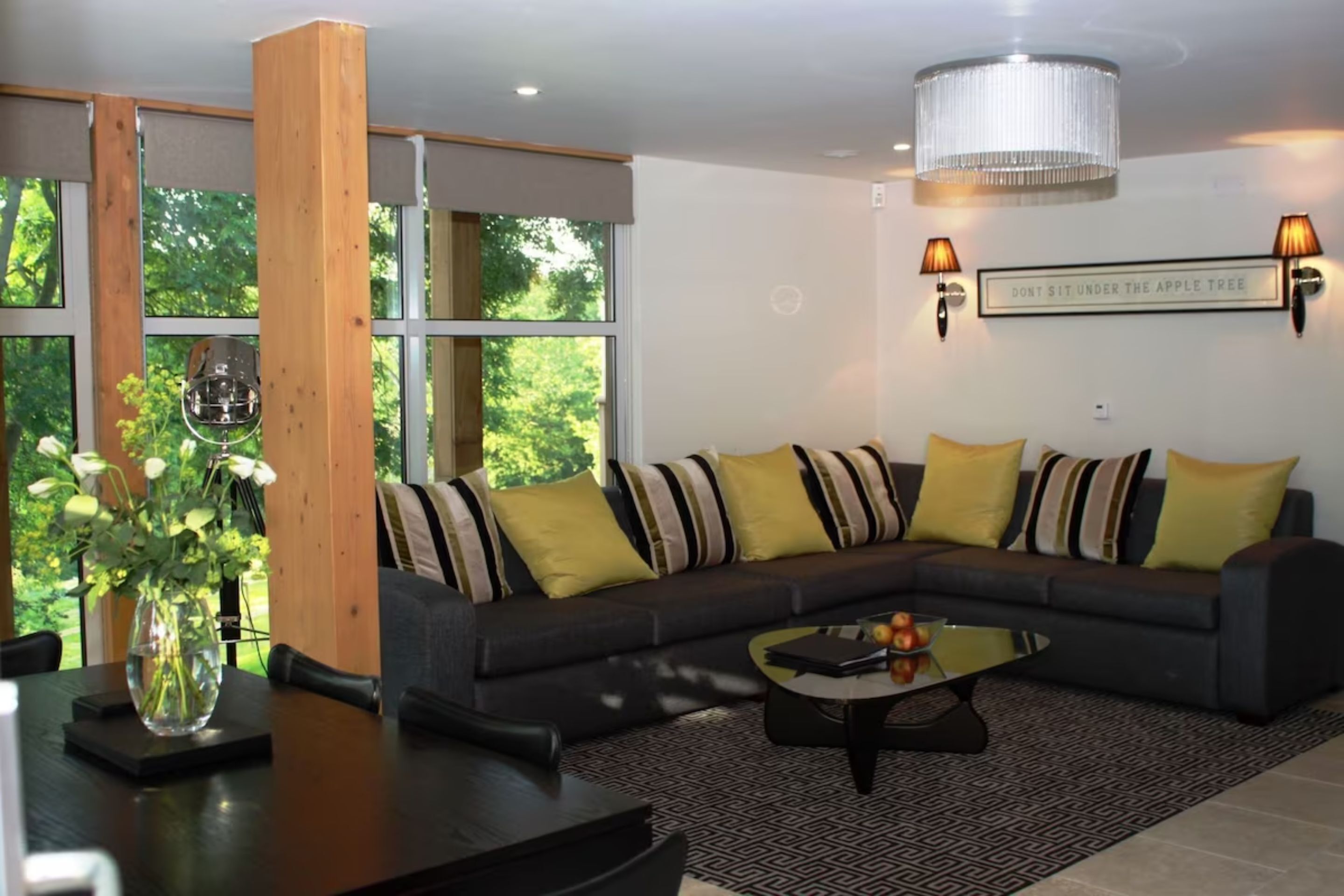 A modern living room with a sectional sofa, a glass coffee table, and a large window with a view of greenery.