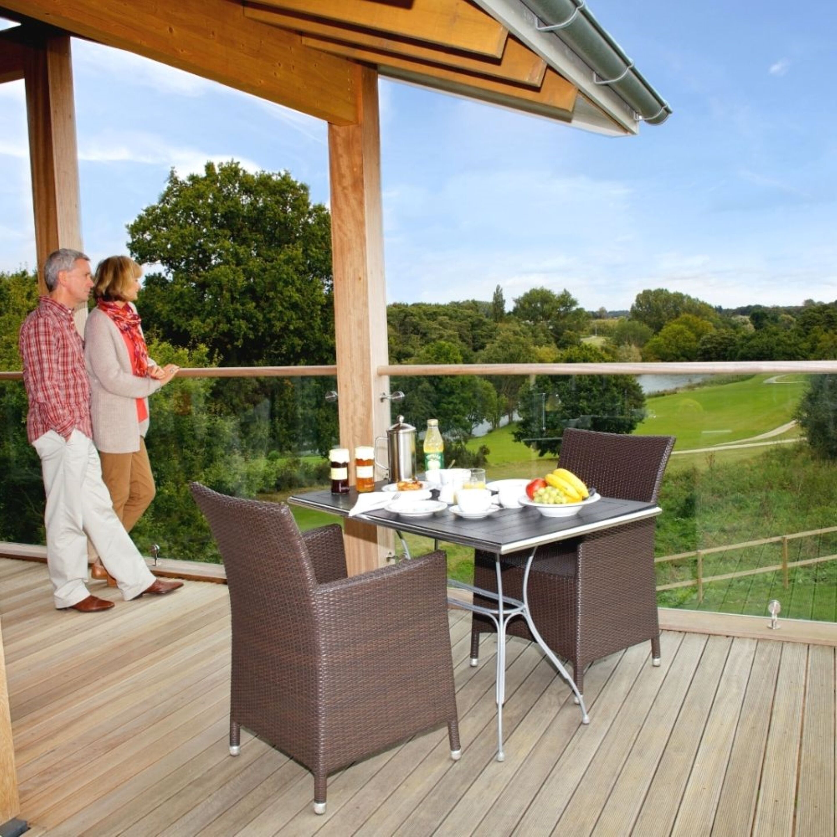 A covered outdoor dining area with wicker chairs and a table set for two, overlooking a scenic landscape.