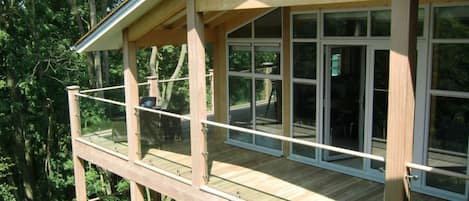 A multi-level wooden deck with glass railings, surrounded by trees.