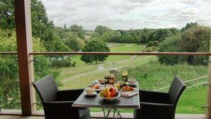 A balcony with a table set for breakfast, overlooking a green landscape. - Apple Tree Lodges (Colchester)