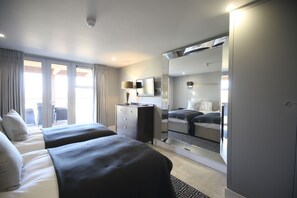 A hotel room with two beds, a dresser, a mirror, and a view of the outside.