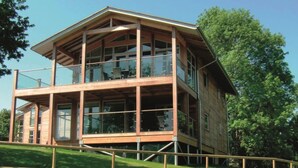 A multi-story wooden building with large windows and balconies, situated on a grassy hill. - Apple Tree Lodges (Colchester)