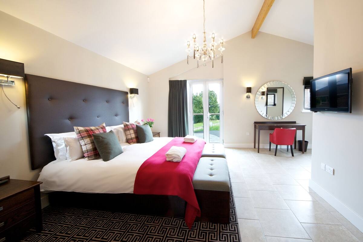 A modern bedroom with a large bed, a red throw blanket, a TV, and a desk with a chair.