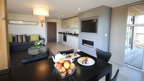 A modern kitchen with a flat-screen TV, a dining area with a table set for breakfast, and a living area with a sofa and cushions. - Apple Tree Lodges (Colchester)