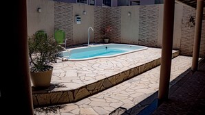 Une piscine aux bords recouverts de pierres, une plante en pot et une structure en forme de pergola.