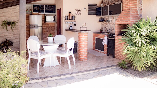 Un espace cuisine extérieur comprenant un four en briques, un réfrigérateur et une table à manger avec des chaises.