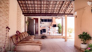 Une terrasse extérieure avec un sol en briques, un canapé marron et un coin repas avec des chaises blanches.