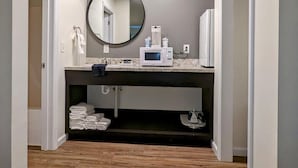 Un baño moderno con tocador, espejo redondo, microondas y barra para toallas.