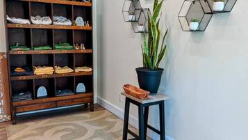 Um corredor com um suporte para sapatos com a etiqueta "HOME", uma planta em vaso e prateleiras hexagonais na parede com pequenas plantas.