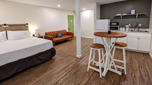 Habitación de hotel con cama, sofá, mesa de comedor con taburetes, kitchenette y una puerta verde.