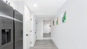 A hallway with a stainless steel refrigerator, white doors, and framed artwork on the walls.