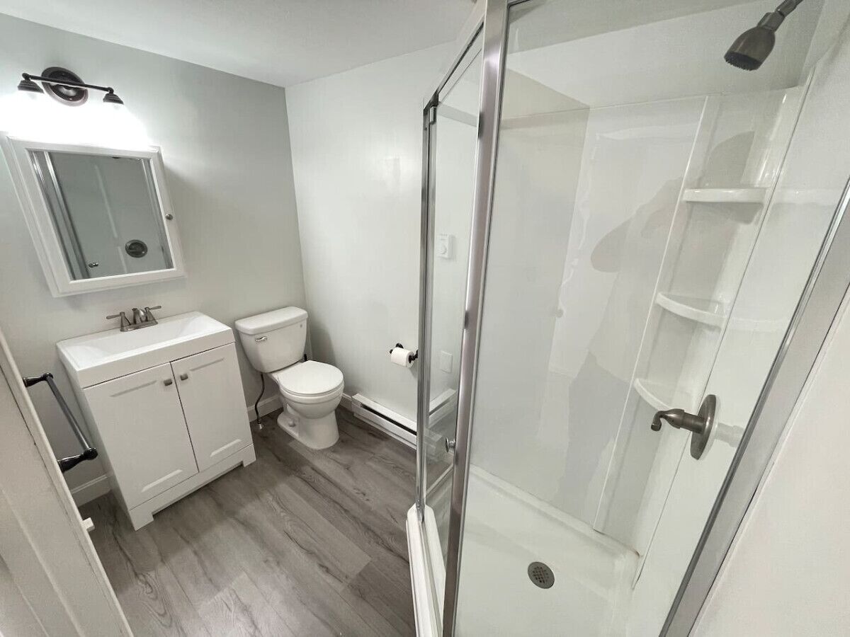 Een moderne badkamer met een douchecabine van glas, een wit wastafelmeubel en een toilet.