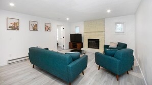 A modern living room with teal sofas, a flat-screen TV, a fireplace, and artwork on the walls.