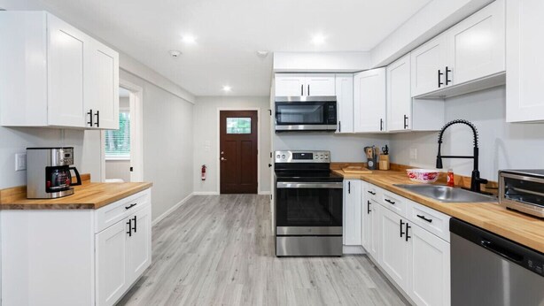 A modern kitchen with white cabinets, stainless steel appliances, and a wooden countertop.