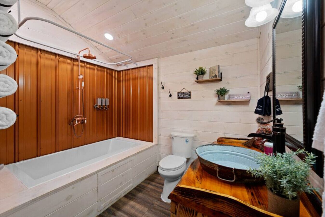 A bathroom with a wooden panel wall, a white bathtub, a white toilet, and a wooden vanity with a sink.