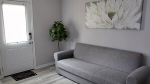 A grey sofa in a room with a white door, a potted plant, and a large white floral painting on the wall. - Private basement w/firepit ideal for longer stays (Suwanee)