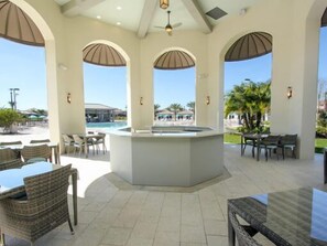 Relax in a serene outdoor space with a central island sink, wicker furniture, and tables under a shaded area.