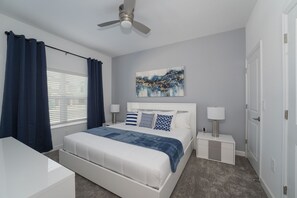 Relax in a serene bedroom with a large bed, nightstand, and dresser, plus a ceiling fan and window with curtains.