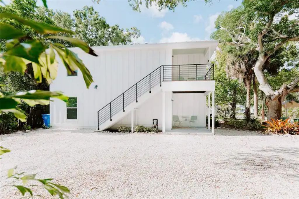 Un bâtiment moderne à l’extérieur blanc, avec un escalier menant à un deuxième étage et un sol recouvert de gravier.