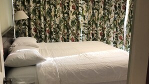 A bedroom with a bed, curtains, a lamp, and a door. - Bayport Residence Inn (Roseau)