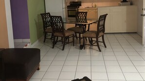 A compact kitchen with white cabinets, a refrigerator, and a microwave. There is a dining table with four chairs. - Bayport Residence Inn (Roseau)