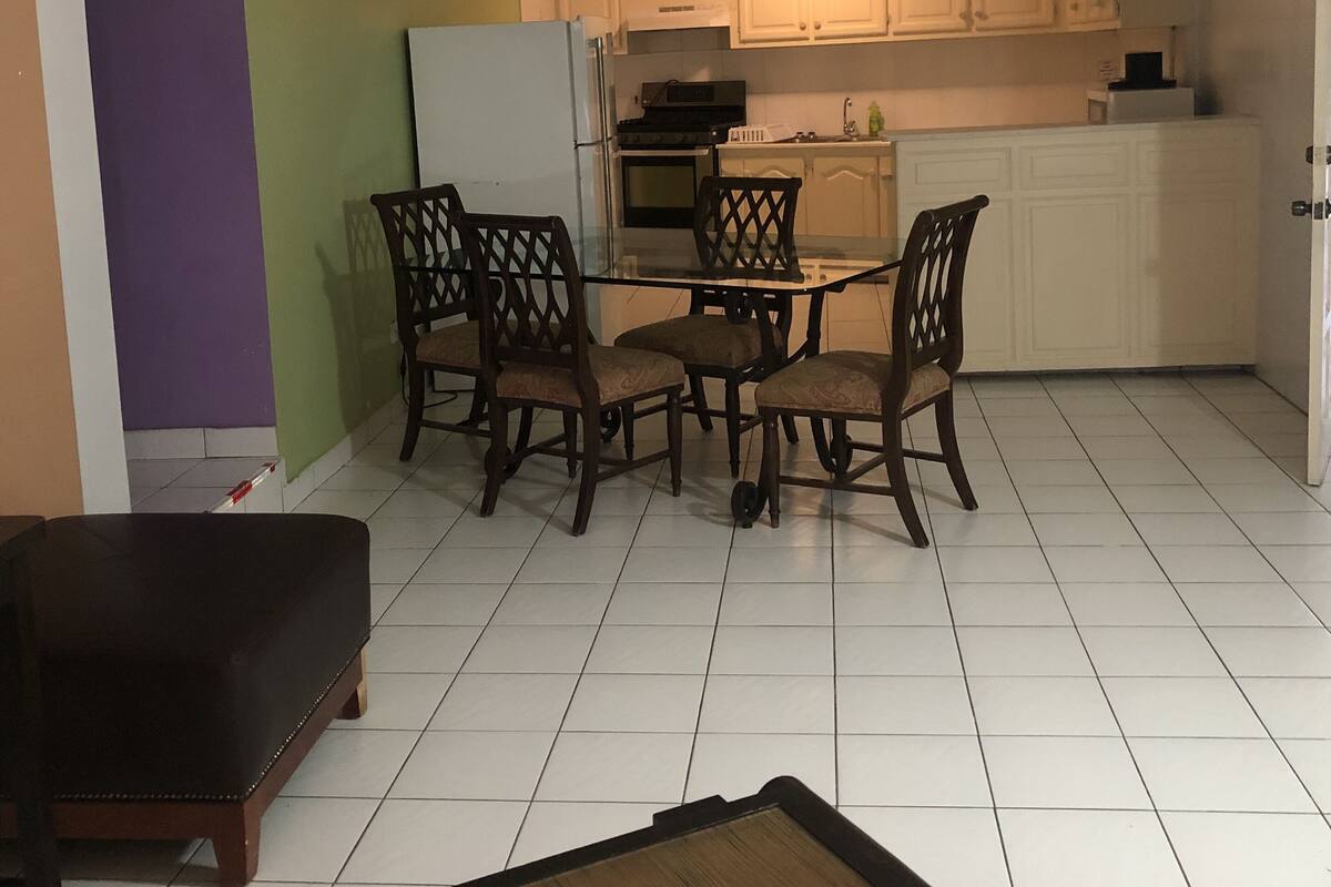 Cocina compacta con armarios blancos, un refrigerador y un microondas. Hay una mesa de comedor con cuatro sillas.