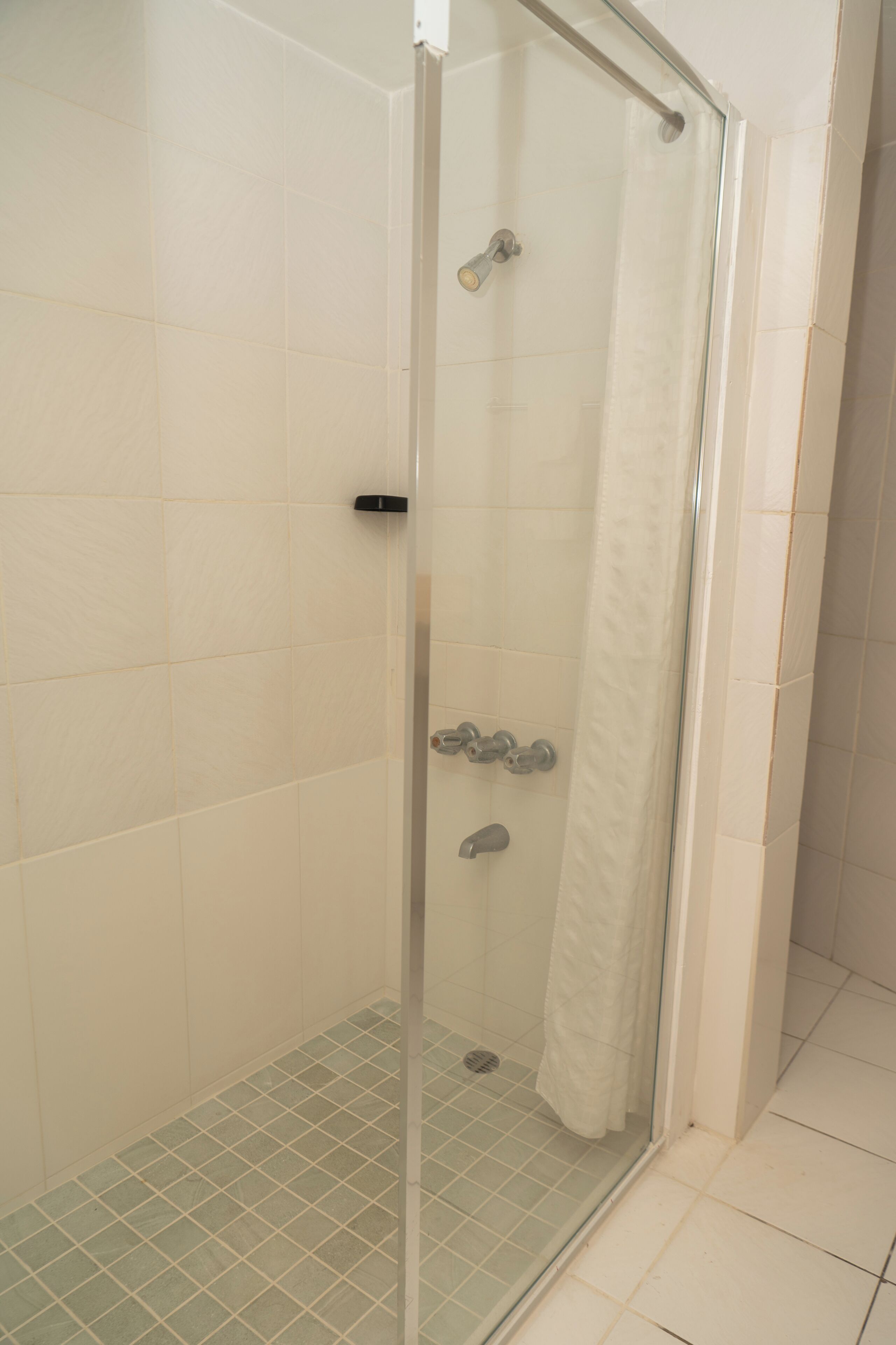 A glass-enclosed shower with a white curtain, tiled walls, and a tiled floor.