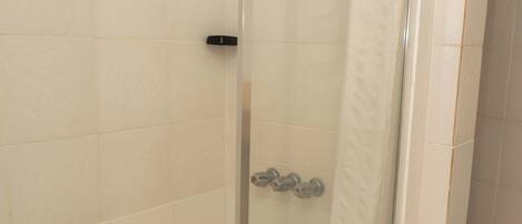 Ducha con cerramiento de vidrio, cortina blanca, paredes y piso cubiertos de azulejos.