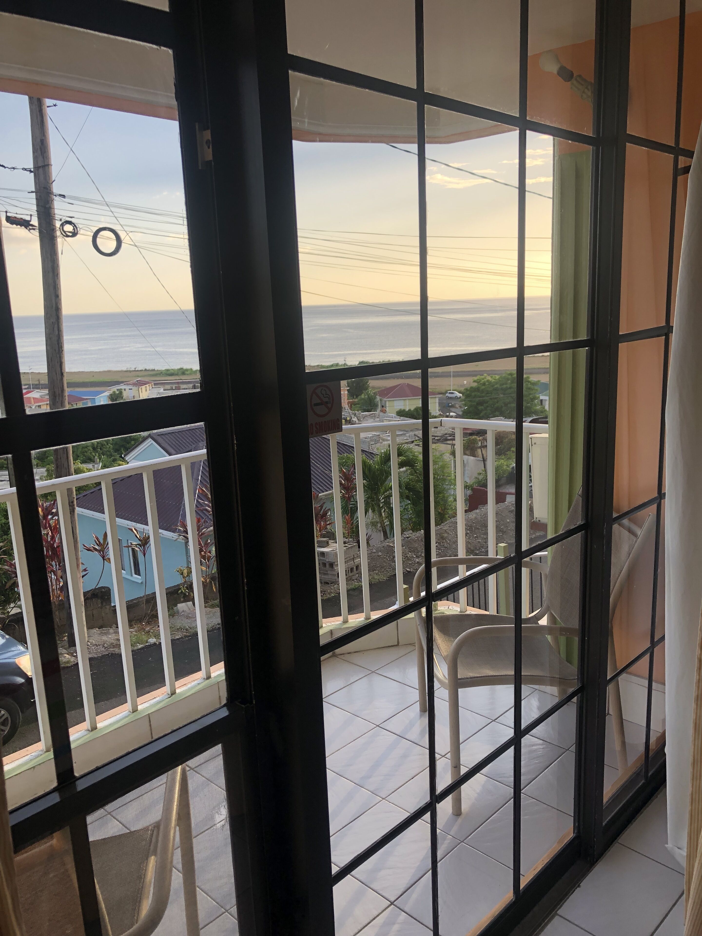 Un balcón con vista al mar, un cartel de prohibido fumar y una silla blanca.