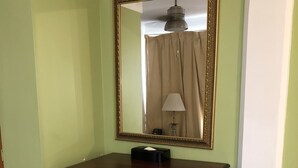 A wooden dresser with a mirror and a lamp in a room with green walls and white tiled flooring. - Bayport Residence Inn (Roseau)