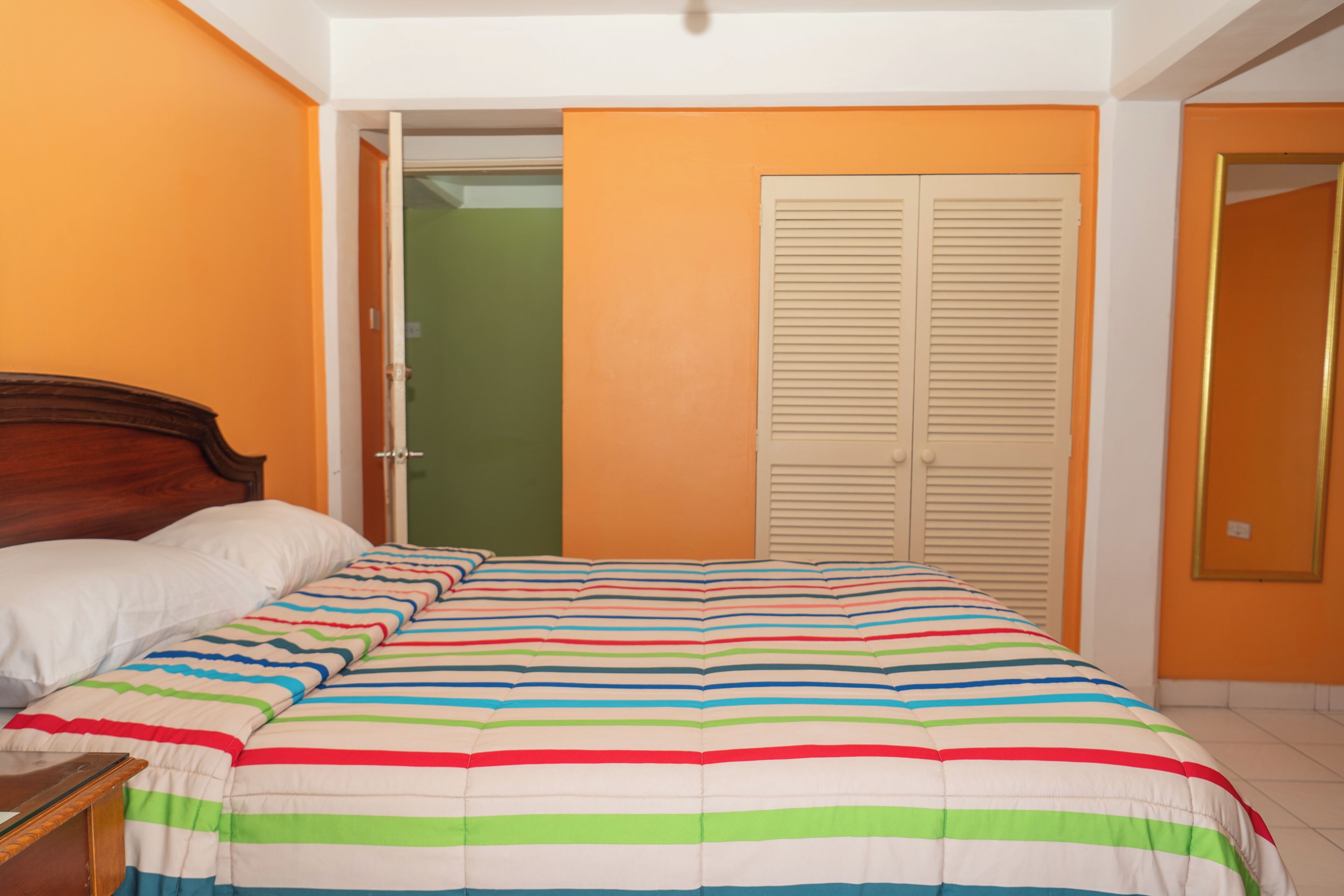 A bedroom with a bed, a nightstand, an open door leading to a green room, and a closet with sliding doors.
