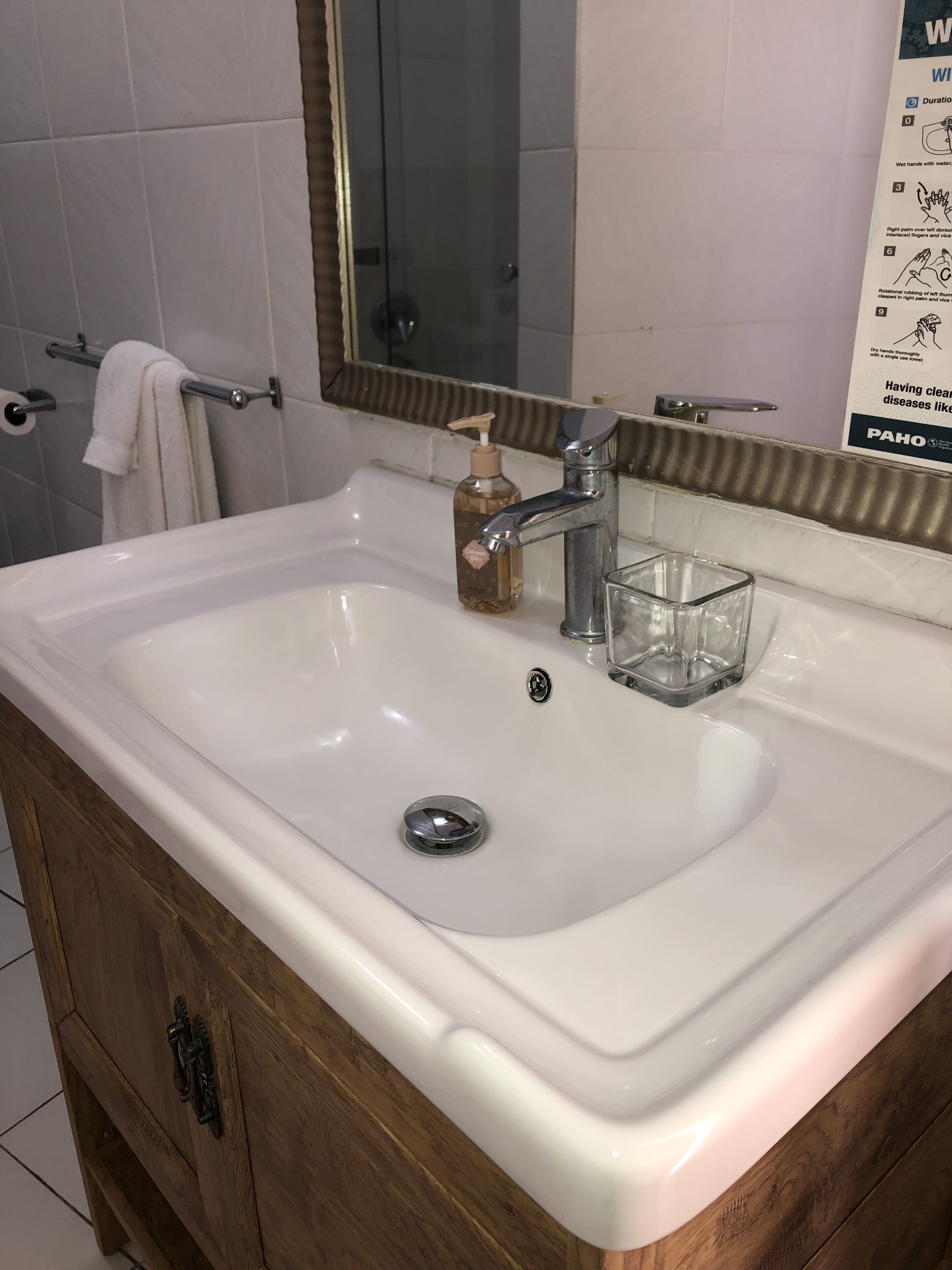 Un baño con un lavamanos blanco, un espejo y un mueble de madera.