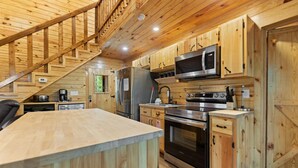 Interior de una cabaña de madera con cocina, que incluye un refrigerador, estufa, microondas y armarios de madera.
