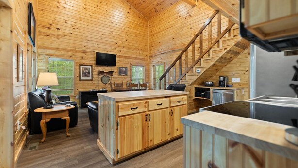 Interior de una cabaña de madera con cocina, comedor y una escalera que sube a un nivel superior.