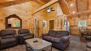 A wooden cabin interior with a dining area, kitchen, and two leather sofas. - Secluded, forested, new cabin, 2-BR, 2-BA, Hot Tub, Wi-Fi, Smart TV's (Campton)