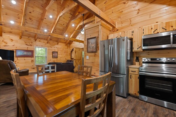 A wooden cabin interior with a dining area, kitchen, and seating space. - Secluded, forested, new cabin, 2-BR, 2-BA, Hot Tub, Wi-Fi, Smart TV's (Campton)