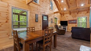 A wooden cabin interior with a dining table, chairs, a sofa, and a television. - Secluded, forested, new cabin, 2-BR, 2-BA, Hot Tub, Wi-Fi, Smart TV's (Campton)
