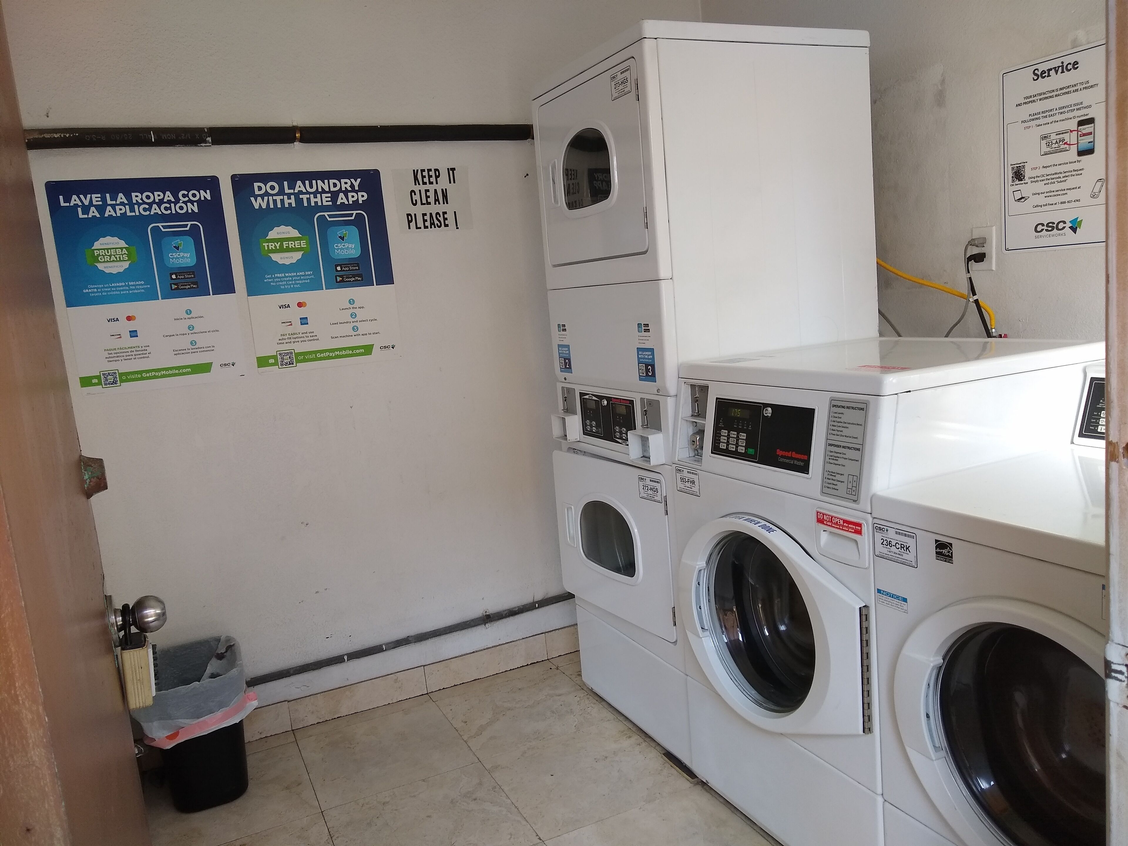 A laundry area with multiple washing machines and dryers, a trash bin, and informational posters on the wall.
