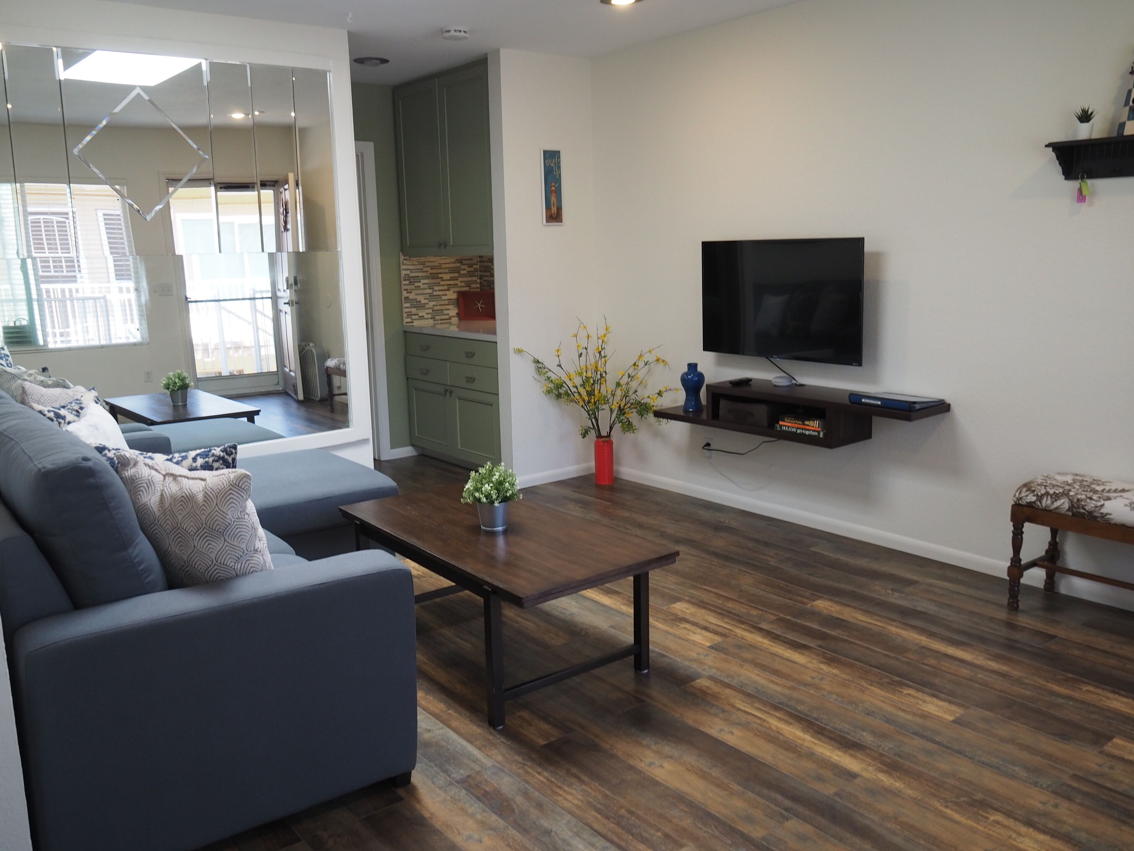 A modern living room with a grey sofa, a wooden coffee table, and a TV mounted on the wall.