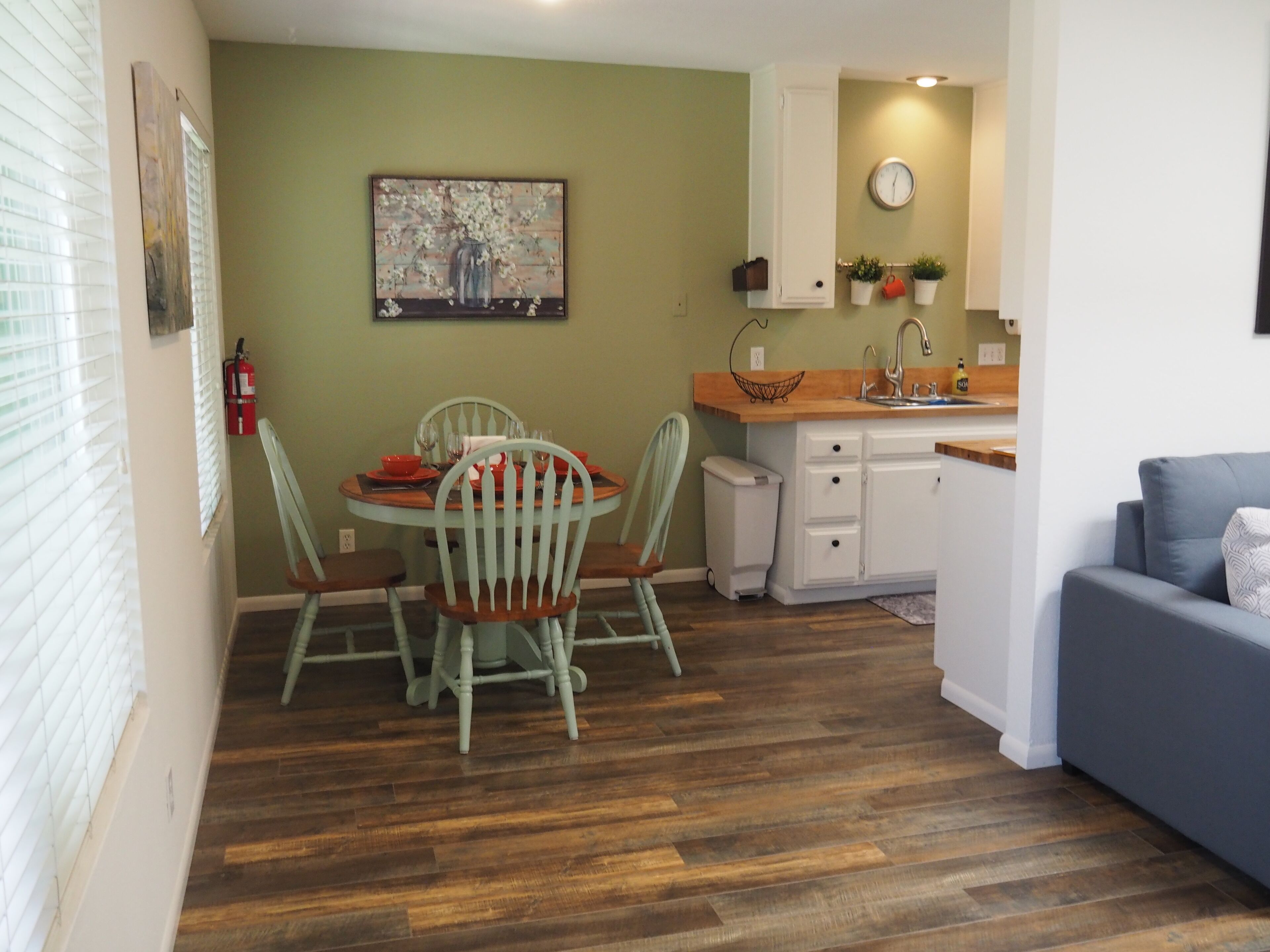 A compact living space with a dining area, kitchenette, and a grey sofa.