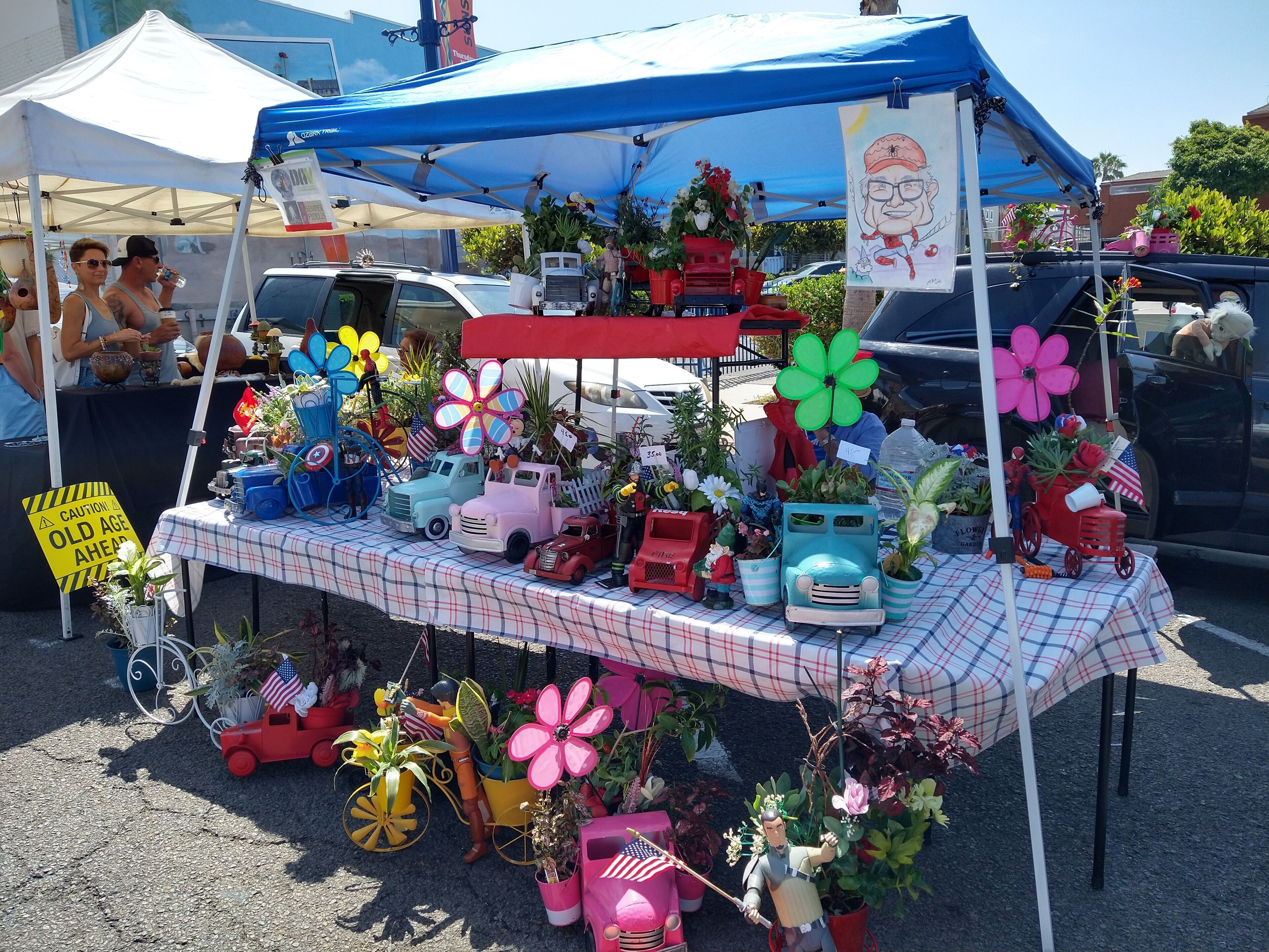 Una mesa con diversos objetos, incluyendo coches de juguete, flores y figuritas, bajo un toldo azul.