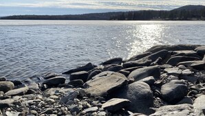 A rocky shoreline with a calm lake and distant forested hills.