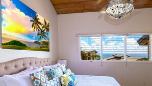 Ein Schlafzimmer mit einem großen Bett, Meerblick durch ein Fenster und einer Wandmalerei mit einer tropischen Strandlandschaft.