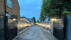 A gated driveway leading to a building with a brick facade and a metal gate. - Cheerful 4 Bedroom Luxury house with free parking (Halesowen)