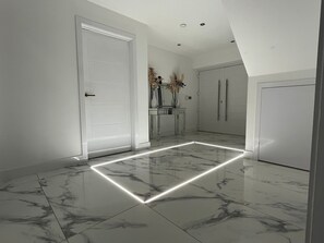 A hallway with a marble floor, white doors, and a vase with flowers on a table. - Cheerful 4 Bedroom Luxury house with free parking (Halesowen)