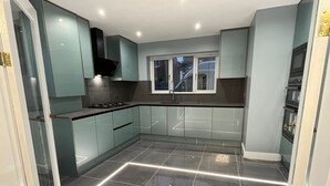 A modern kitchen with grey cabinets, a stainless steel stove, and a window above the sink. - Cheerful 4 Bedroom Luxury house with free parking (Halesowen)