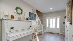 Un pasillo amplio con una consola blanca, una escalera y una puerta que dice "WELCOME".