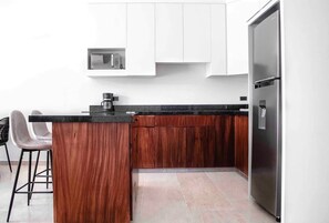 Una cocina compacta con microondas integrado, cafetera y refrigerador de acero inoxidable.