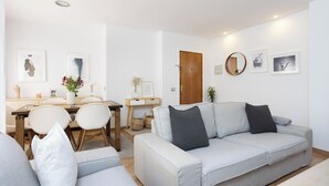 Een moderne woonkamer met een bank, een eettafel met stoelen en kunstwerken aan de muur.